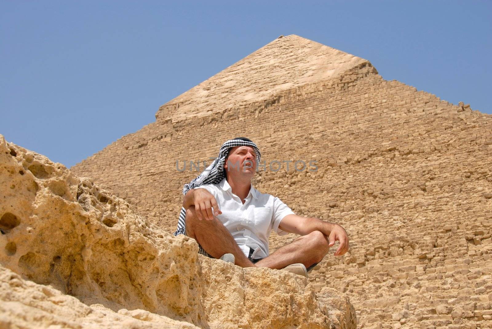 caucasian man tourist in arabic kerchief sitting by pyramids on Giza in Egypt
