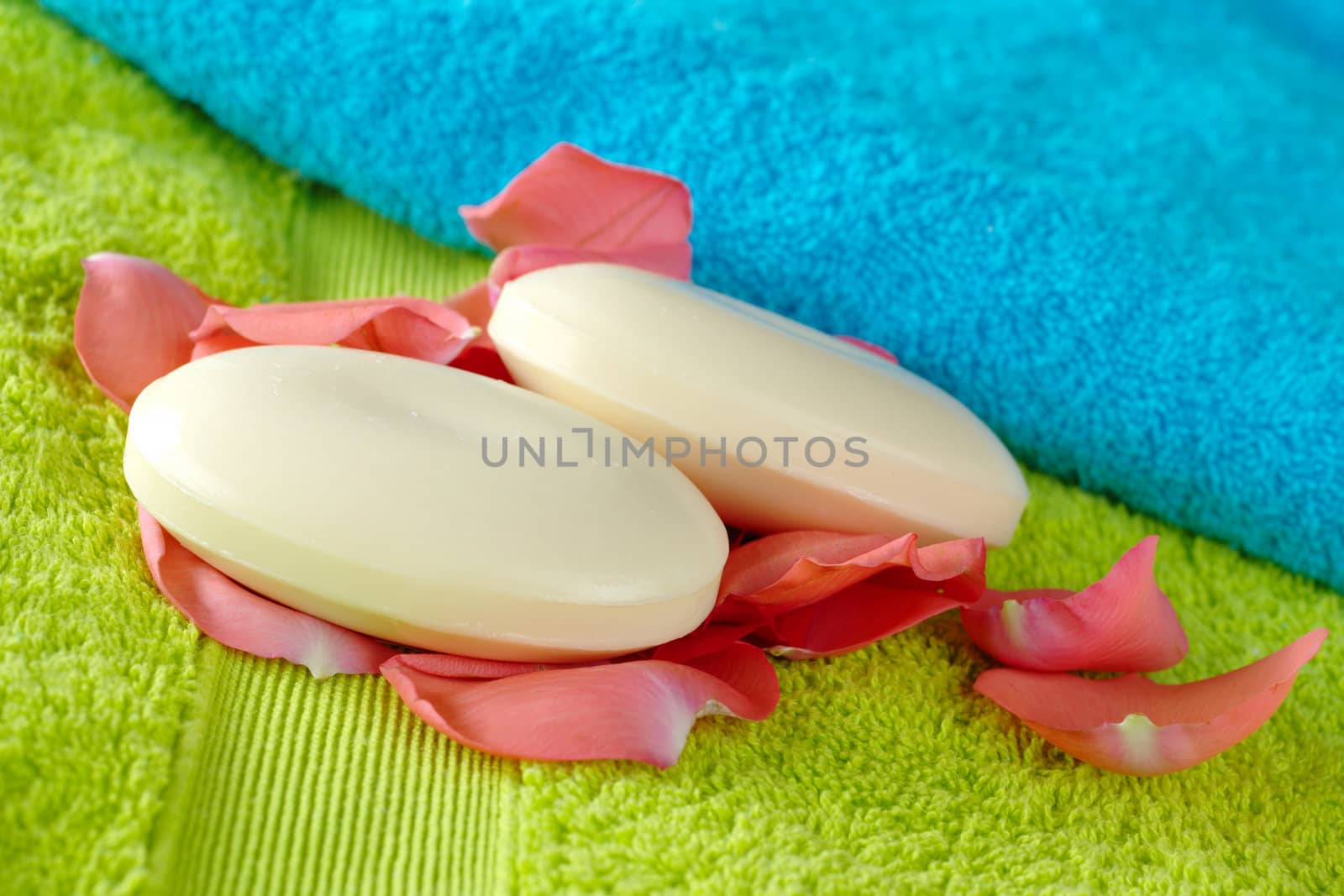 Blue and green bath towels with white soaps between pink rose petals (Selective Focus, Focus on the front soap)