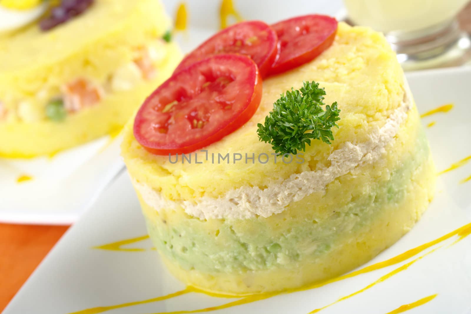 Peruvian dish called Causa, which is made of mashed yellow potatoes, and here, filled with avocado and chicken (Selective Focus, Focus on the parsley and the front of the meal) 