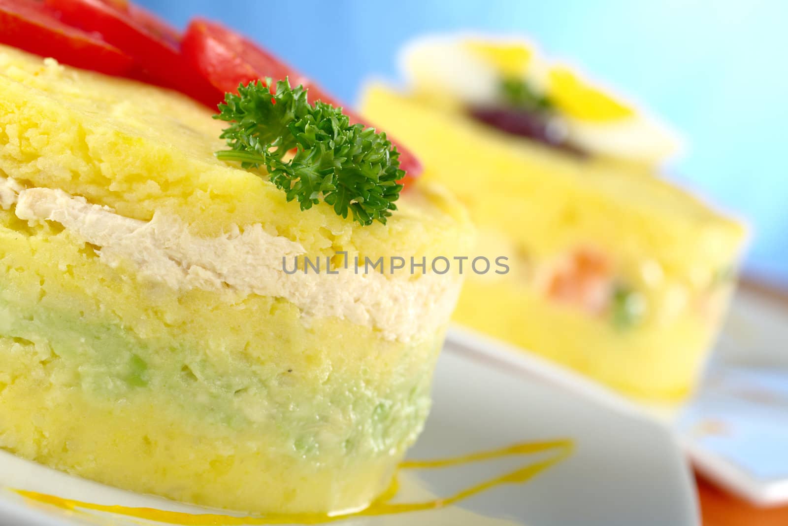 Peruvian dish called Causa, which is made of mashed yellow potatoes, and here, filled with avocado and chicken (Selective Focus, Focus on the parsley and the front of the meal) 