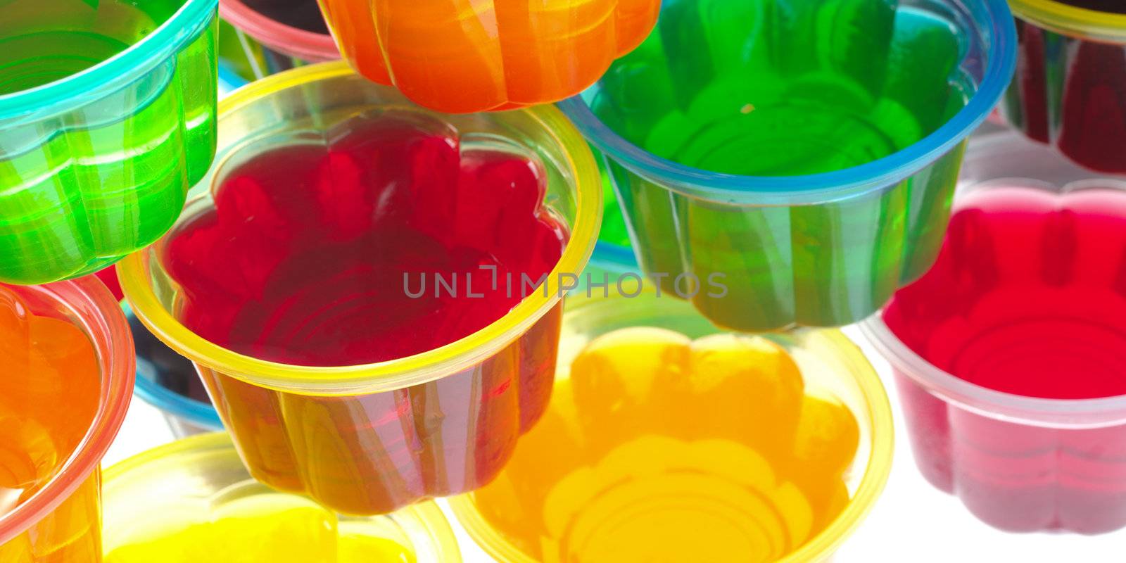 Colorful jellies in plastic bowls arranged in a pile and photographed from above (Selective Focus, Focus on the rim of the left red jelly) 