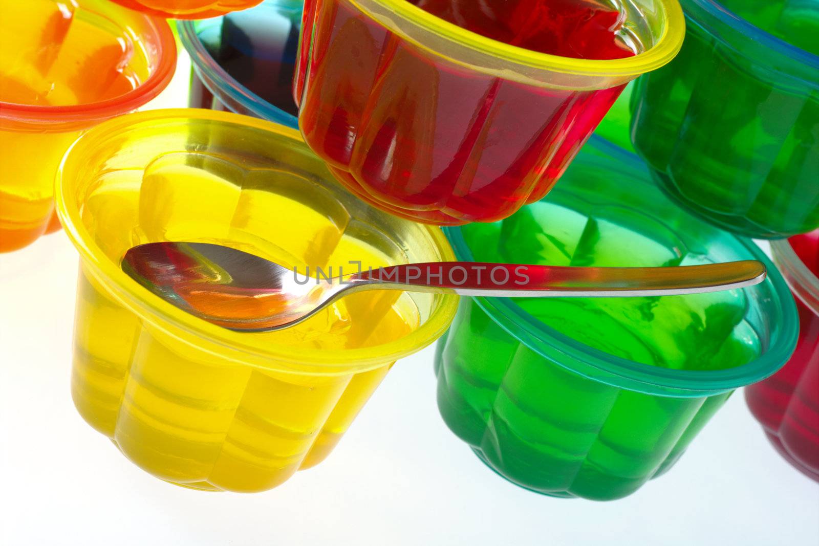 Colorful jellies in plastic bowls arranged in a pile with a teaspoon (Selective Focus, Focus on the teaspoon) 