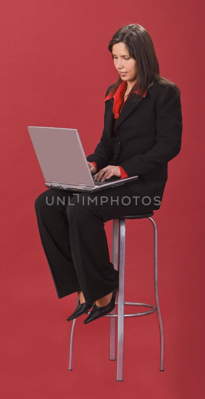 Young businesswoman working on a laptop while sitting on a high chair.