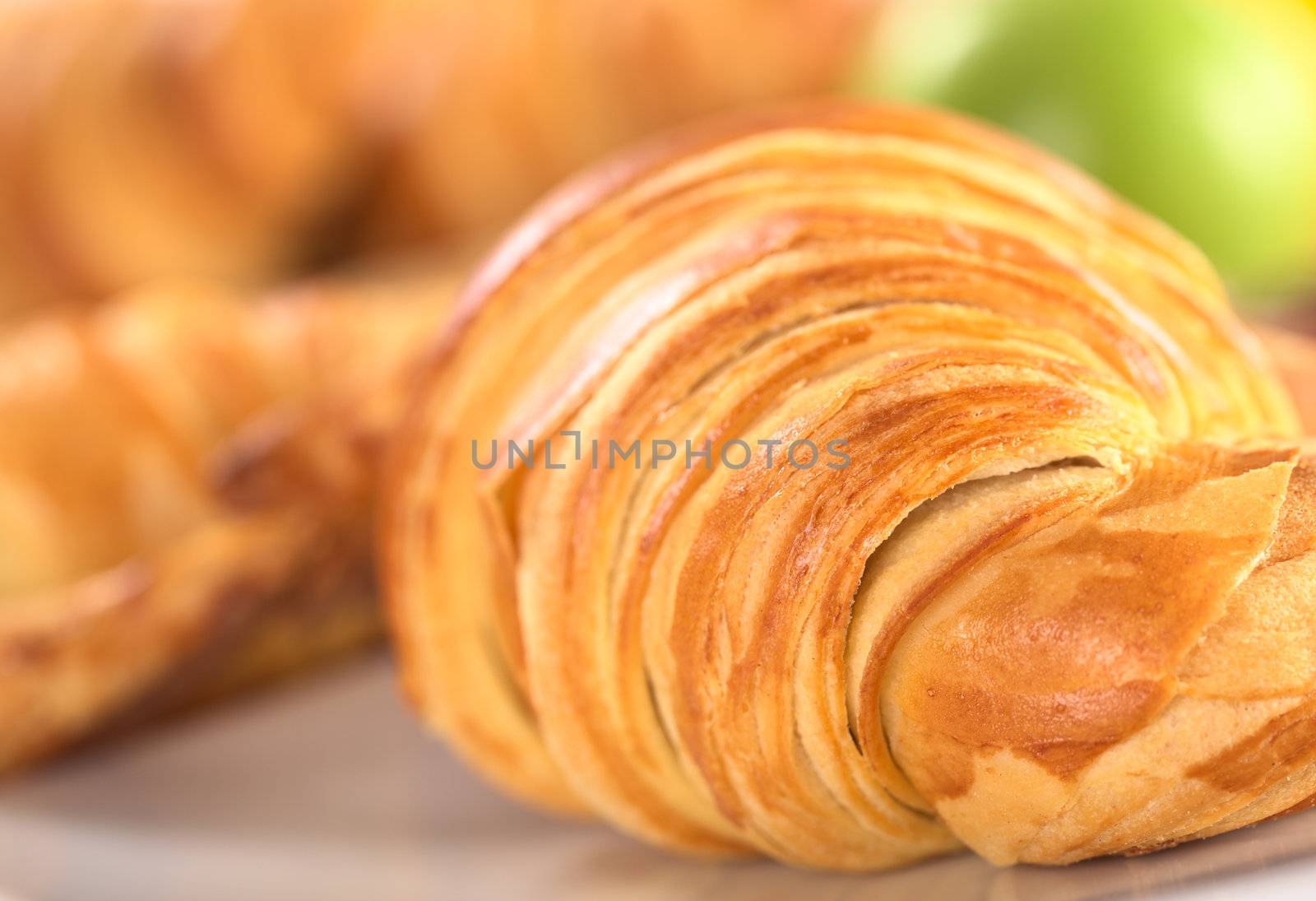 Closeup of a croissant with a green apple in the background (Selective Focus, Focus one third into the right croissant)