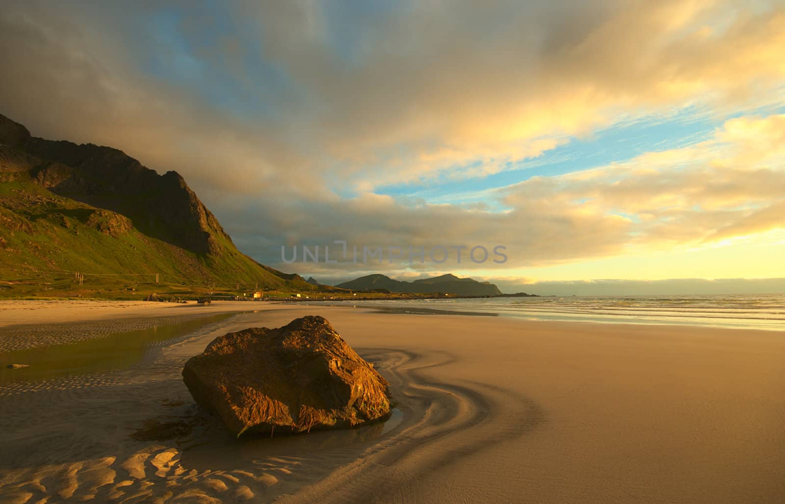 Rock on a sandy beach on the island of  Flakstadoya, Lofoten, Norway lit by the yellow midnight sun in July 