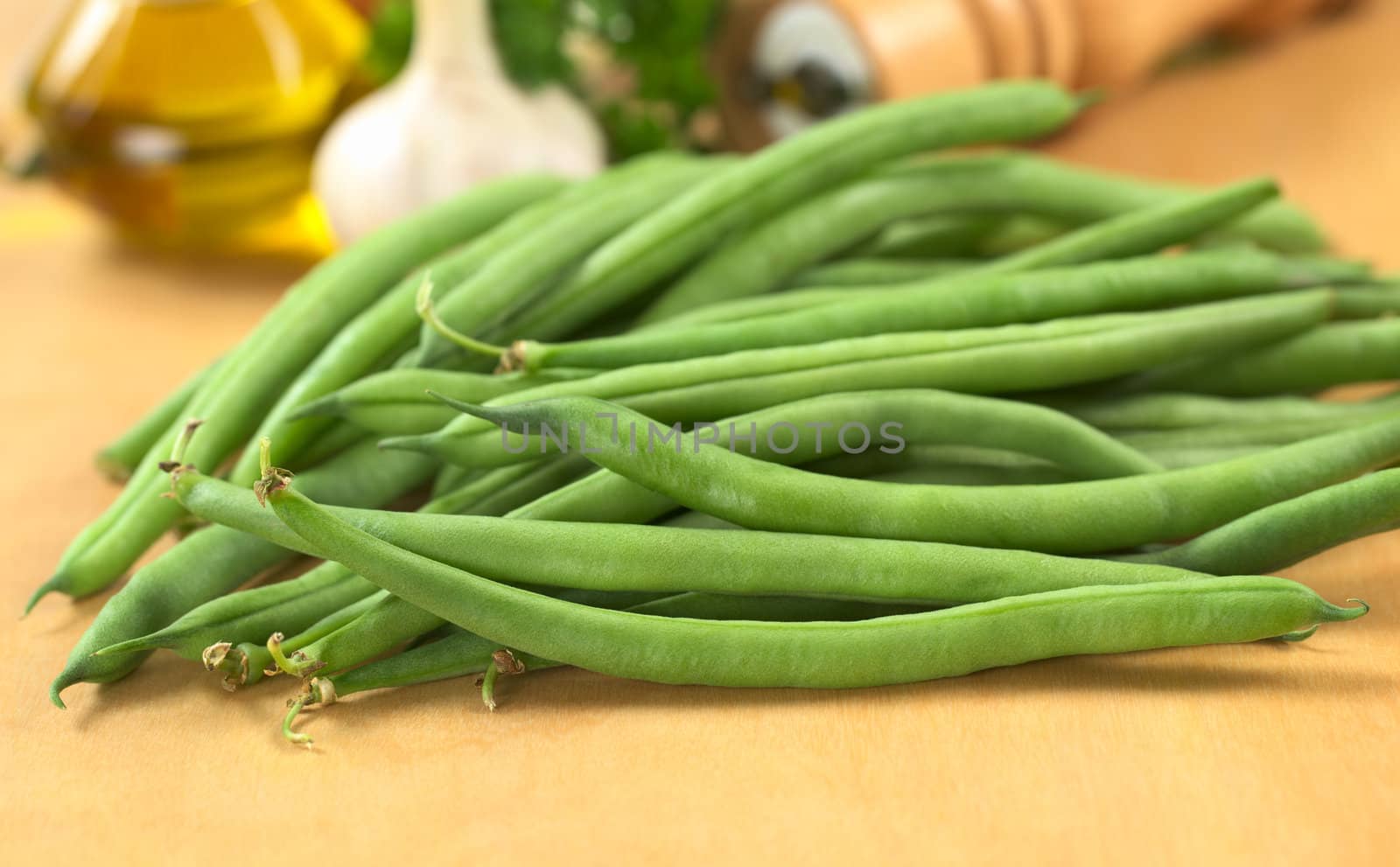 Fresh raw green beans on wooden board with oil, garlic, parsley and pepper mill in the back (Selective Focus, Focus on the bean in the front)
