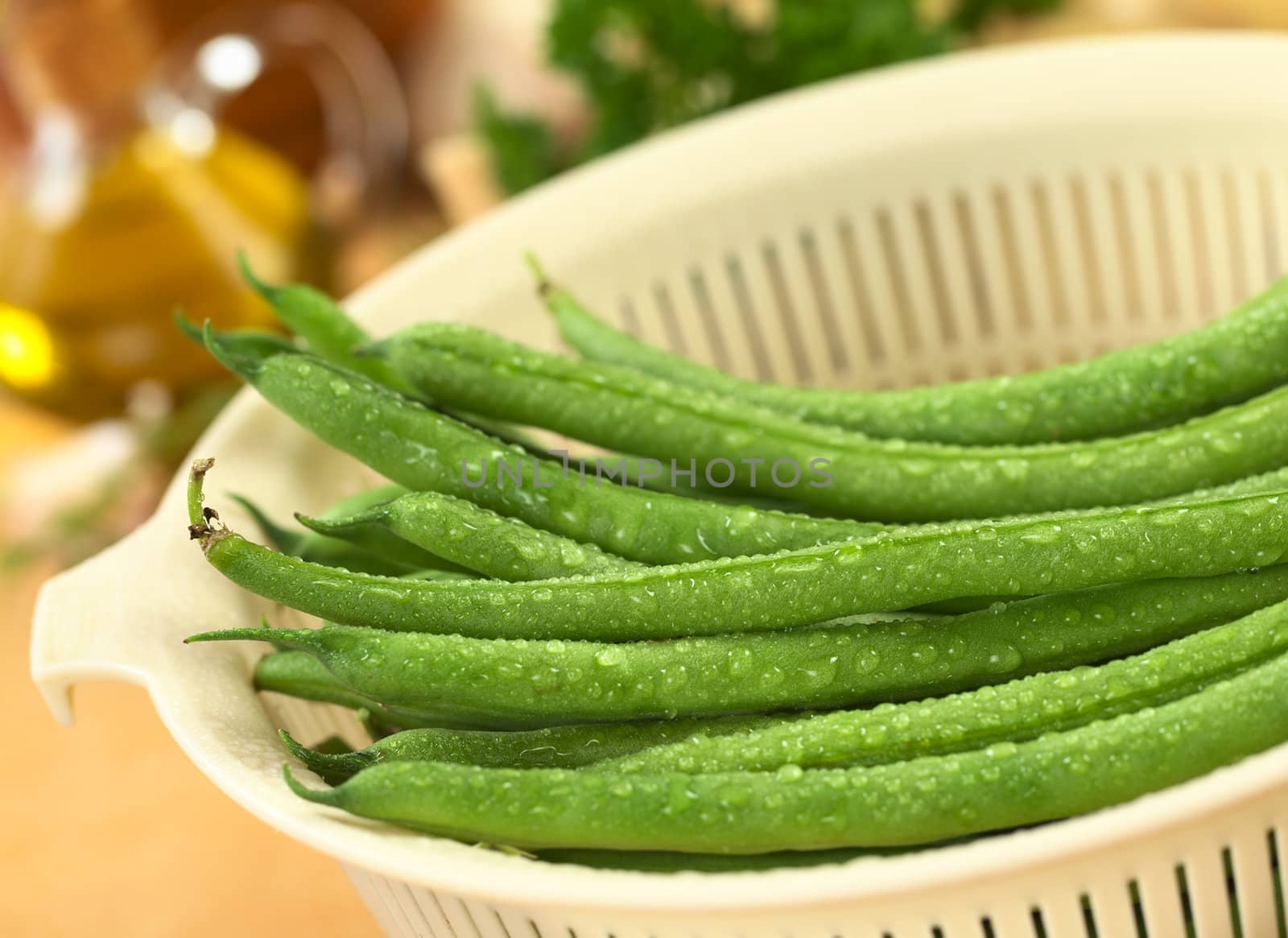 Fresh raw green beans sprinkled with water in plastic strainer (Selective Focus, Focus on the bean in the middle)