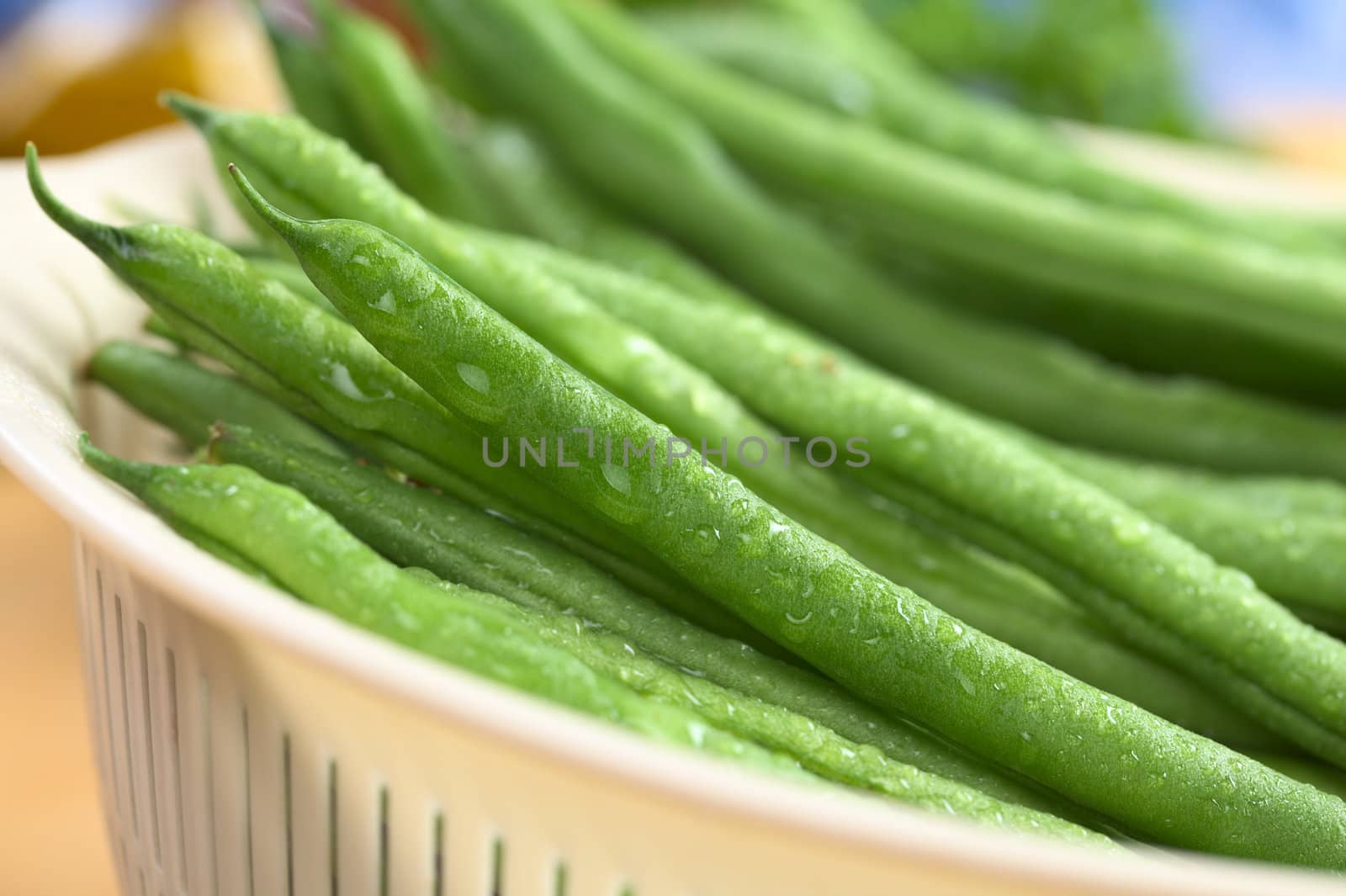 Fresh raw green beans sprinkled with water in plastic strainer (Selective Focus, Focus on the bean one third into the strainer)