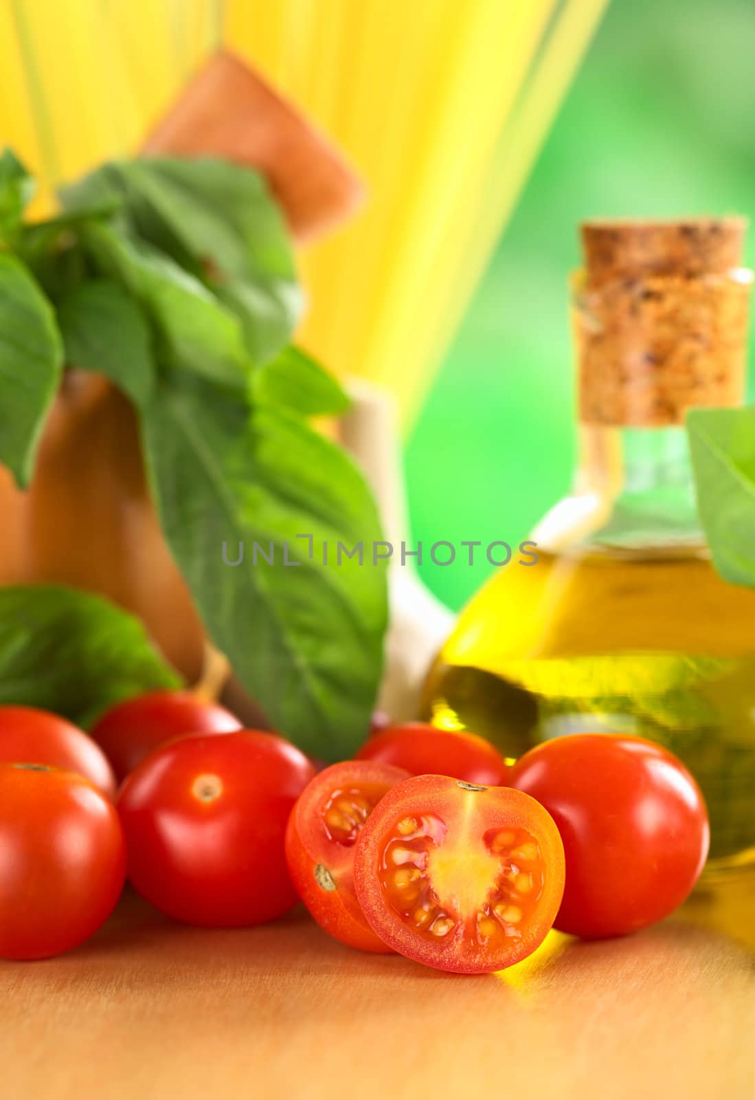 Cherry tomatoes on wooden board with other ingredients such as olive oil, garlic, spaghetti and basil with a wooden mortar (Selective Focus, Focus on the first tomato half)