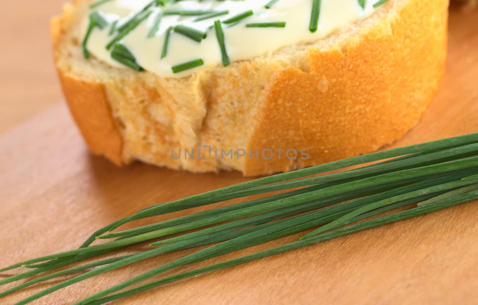 Fresh chives on cutting board with a baguette slice, soft cheese and chives in the back (Selective Focus, Focus one third into the chives)