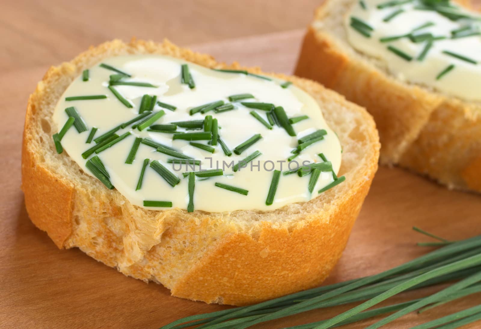 Baguette slices with soft cheese and chives on cutting board (Selective Focus, Focus on the front of the first baguette)