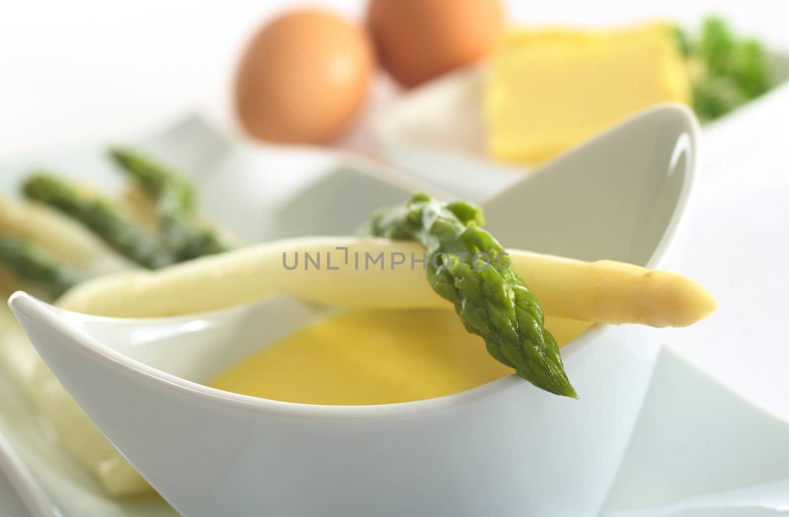 Asparagus lying on a bowl full of Hollandaise sauce (Very Shallow Depth of Field, Focus on the head of the green asparagus)