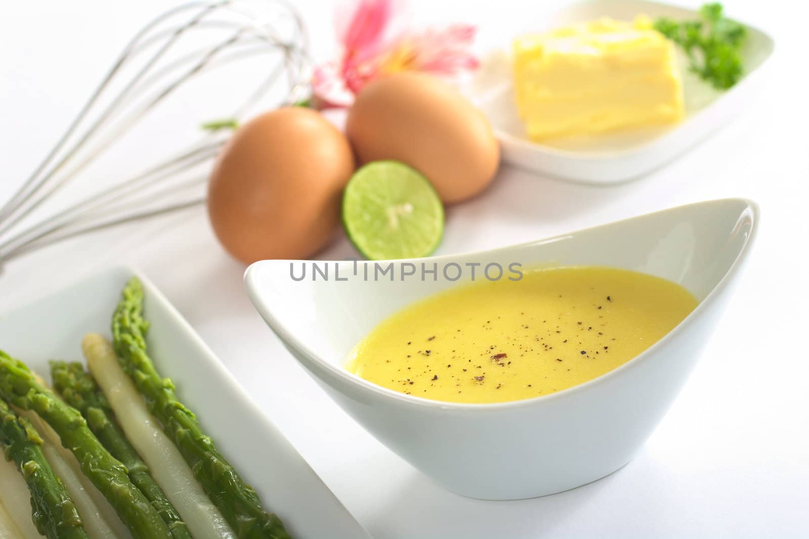 Hollandaise sauce with black pepper, asparagus on the side and the ingredients (butter, egg, lemon) of the sauce in the back (Selective Focus, Focus in the middle of the bowl)