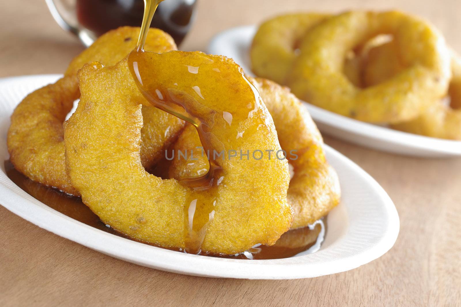 Pouring Chancaca syrup (kind of honey) on the popular Peruvian dessert called Picarones made from squash and sweet potato, served on plastic plate (Selective Focus, Focus on the front)