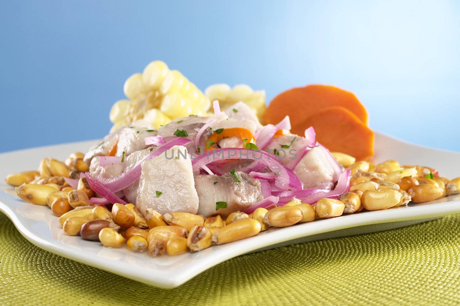 Peruvian-style ceviche made out of raw mahi-mahi fish (Spanish: perico), red onions and aji (Peruvian hot pepper) and served with roasted corn (cancha) and cooked corn cob as well as cooked sweet potato (Selective Focus, Focus on the front of the fish)