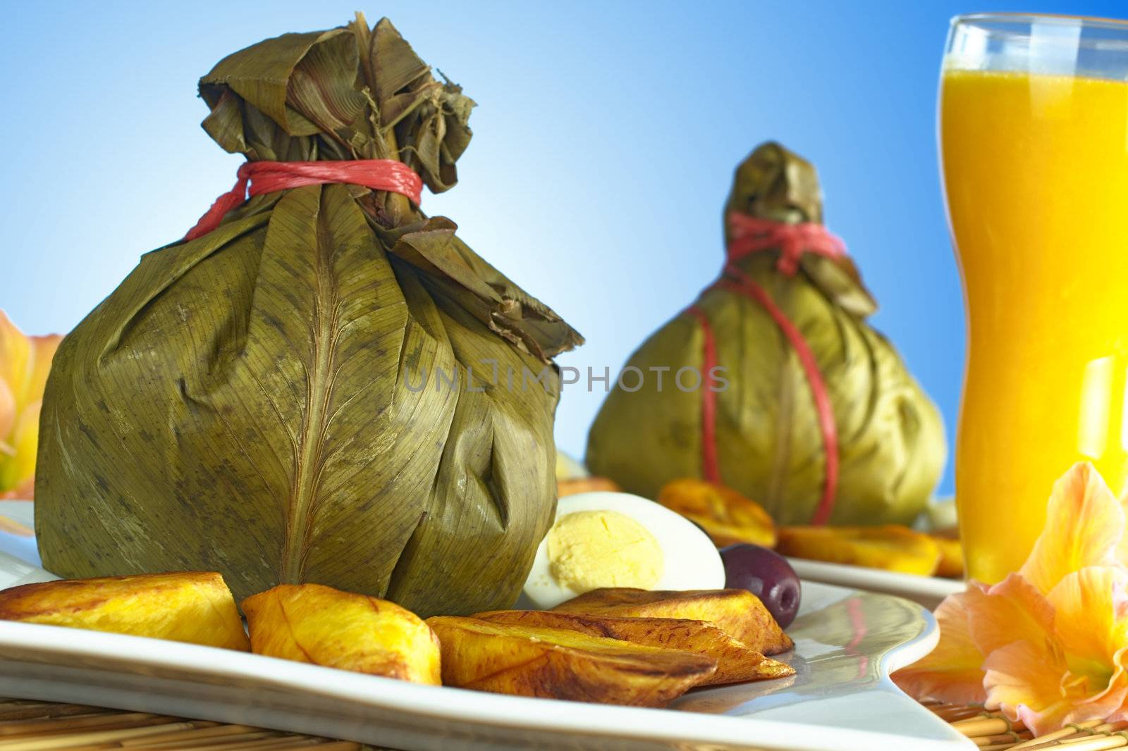 Traditional Peruvian food called Juane from the jungle area, in which rice, eggs and different kind of meat is wrapped into bijao leaves, and is served with fried plantains, eggs and black olives. On the side a mango juice is standing. (Selective Focus, Focus on the front)