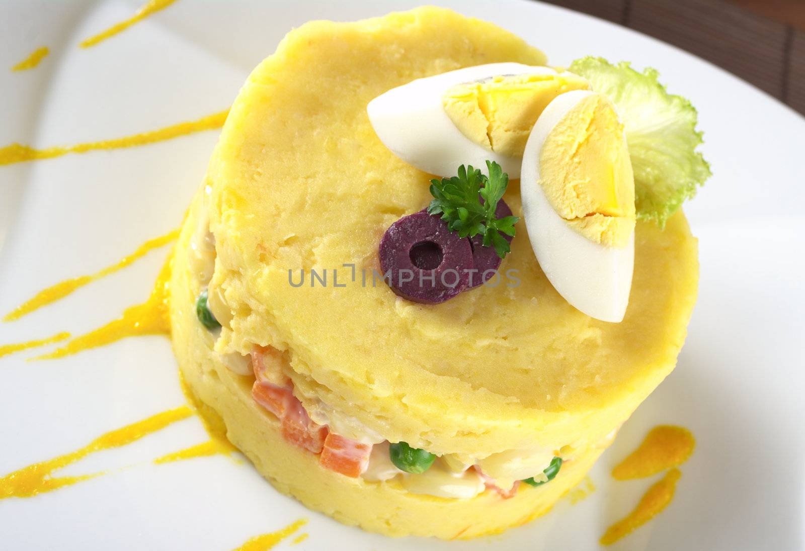 Traditional Peruvian dish called Causa made of mashed yellow and white potato mixed with aji (hot pepper) and lime juice and filled with vegetables (corn, peas, carrots) and mayonnaise and garnished with eggs and olives (Selective Focus, Focus on the olives and the top) 