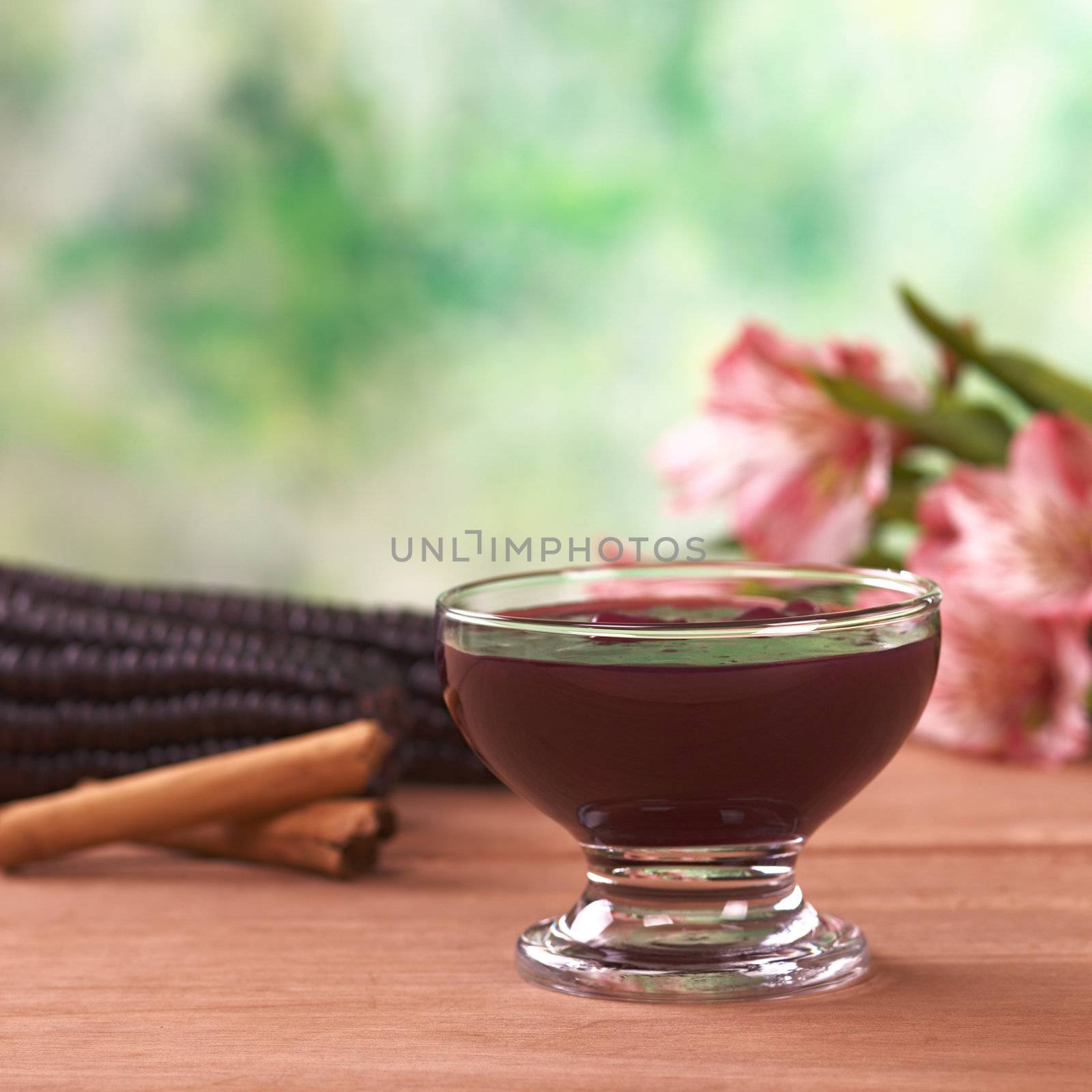 Popular Peruvian dessert called Mazamorra Morada (made out of purple corn) with cinnamon sticks and pink inca lily in the back (Selective Focus, Focus on the front of the bowl)