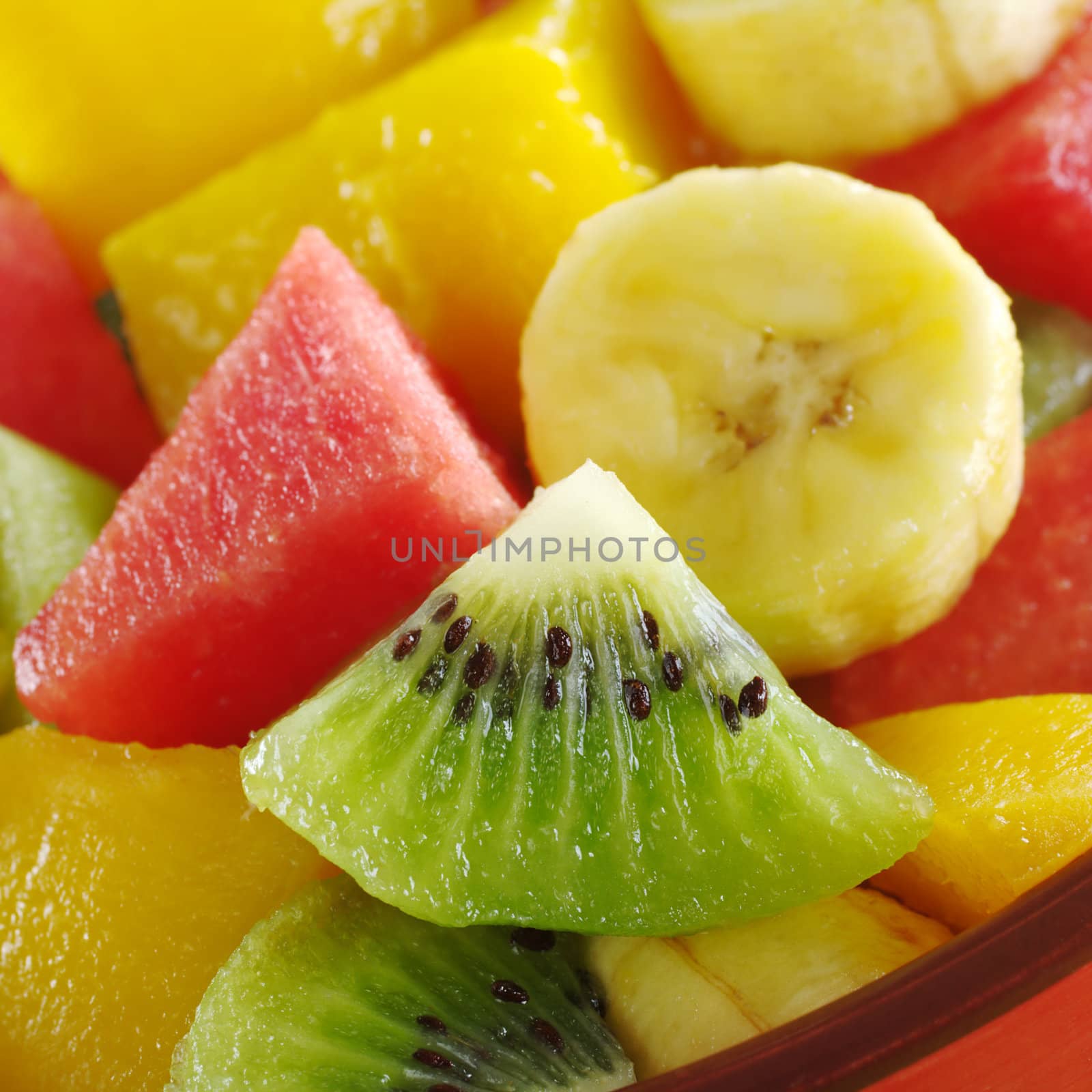 Fresh and healthy tropical fruit salad out of kiwi, mango, banana and watermelon pieces in an orange bowl (Selective Focus, Focus on the kiwi slice)