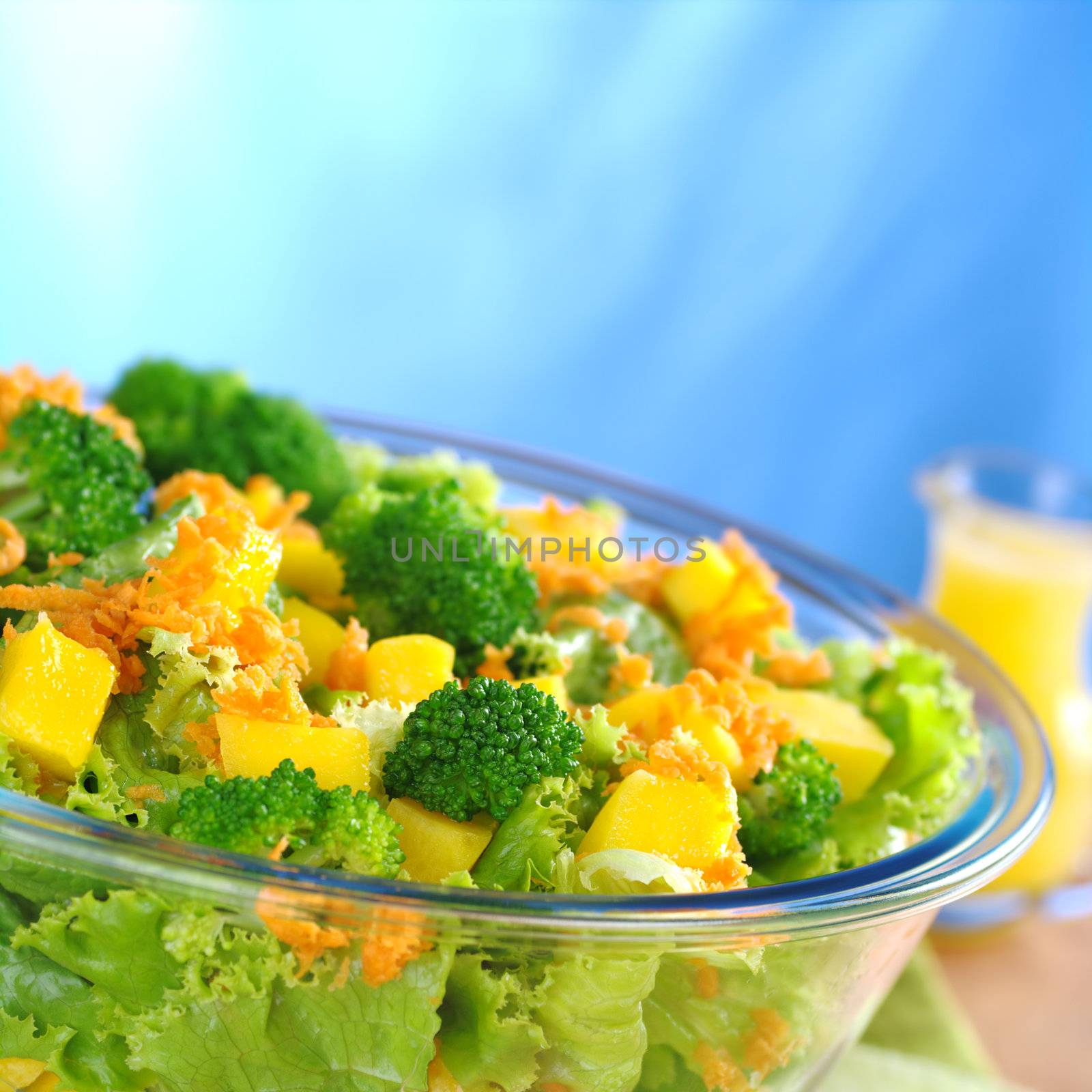 Broccoli-mango-carrot-lettuce salad in a glass bowl with orange juice dressing in the background (Selective Focus, Focus on the front)