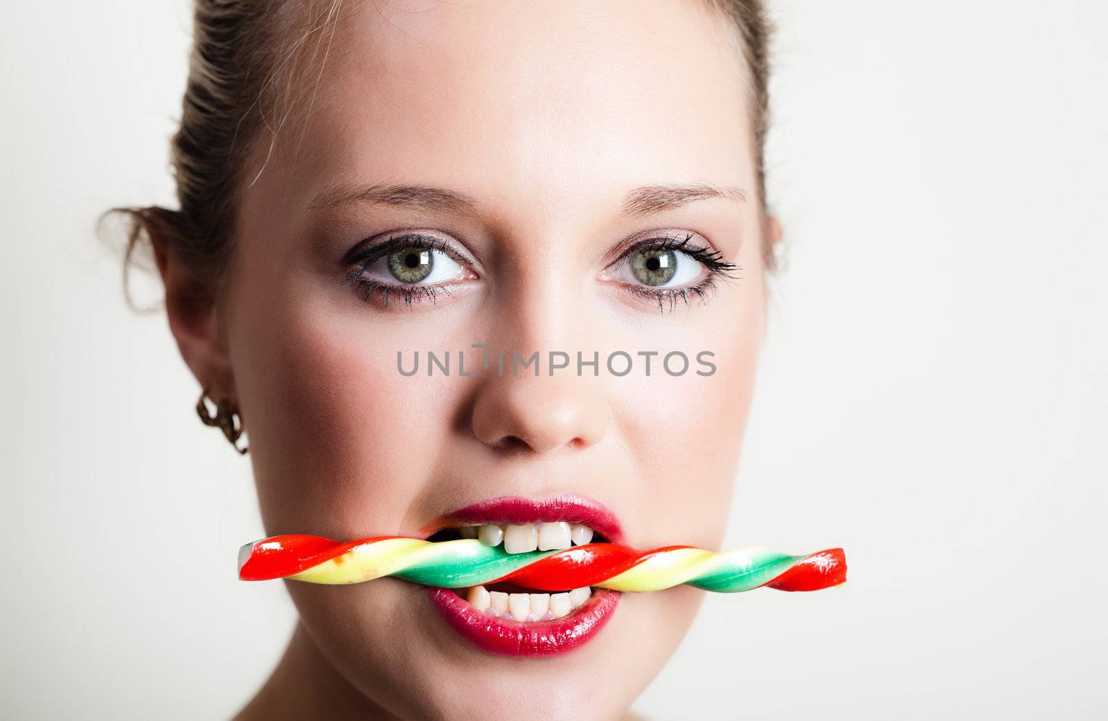 Portait of young woman holding colorful candy in her teeth