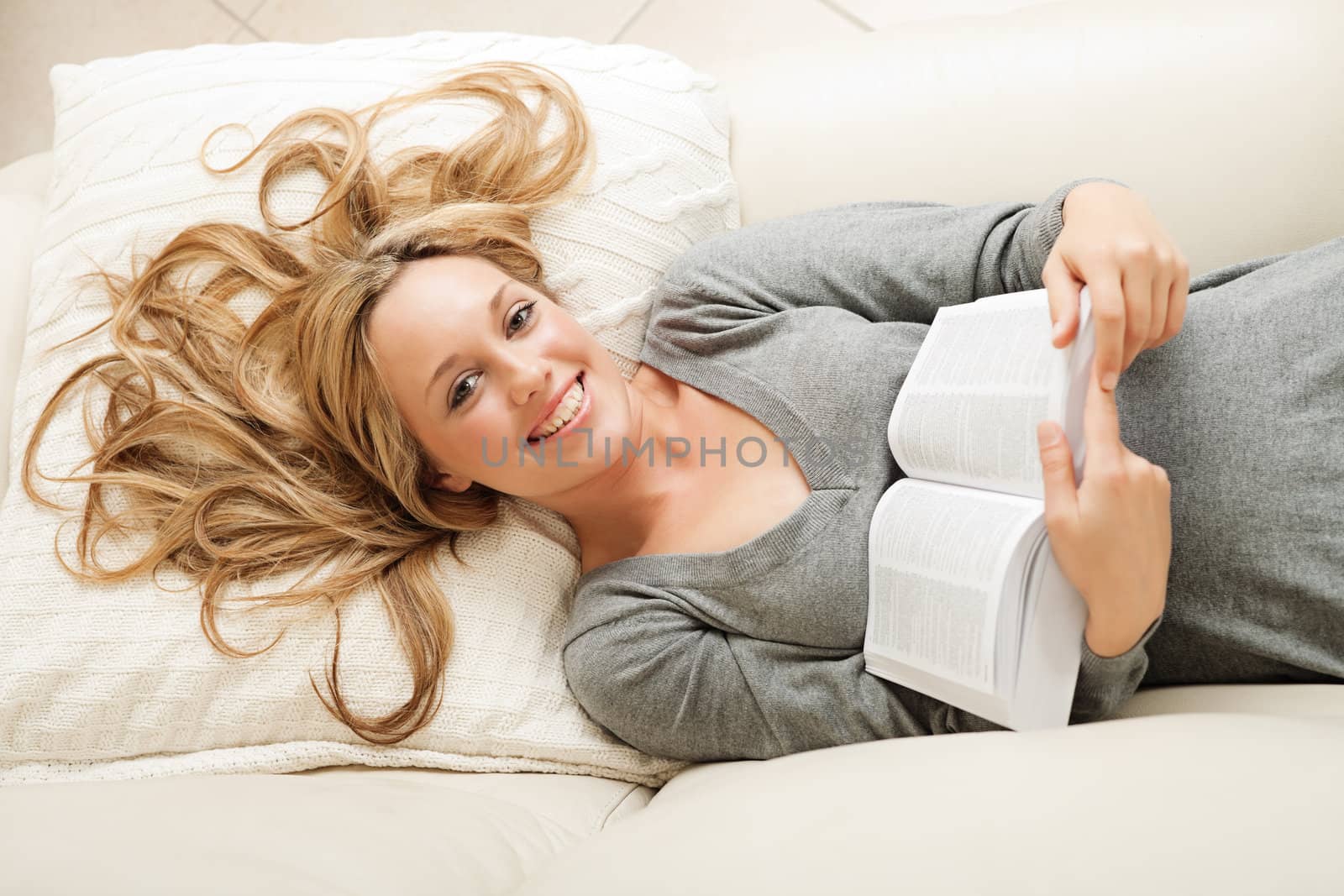 High angle view on smiling blond woman lying on sofa with book