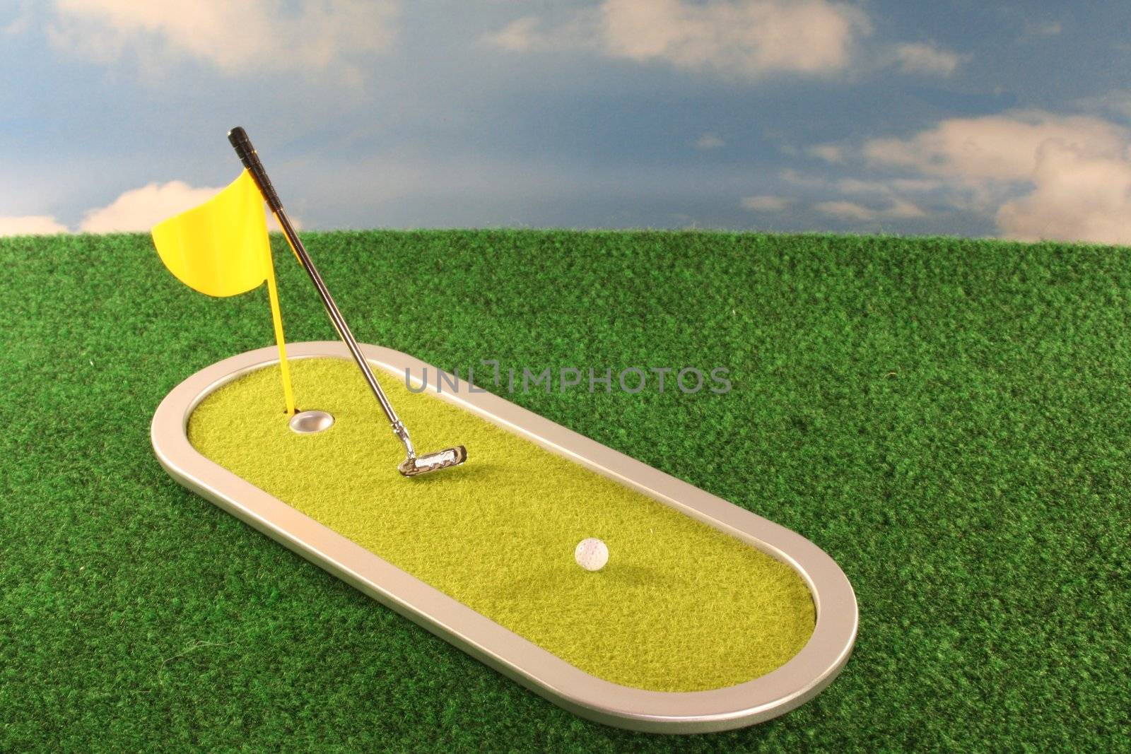 Golf game with putter, golf ball and a flag on the lawn before a blue sky