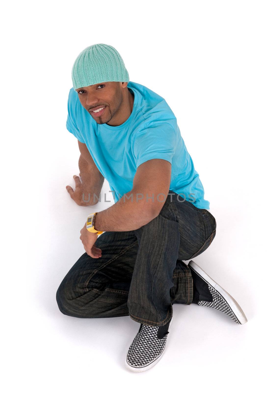 Relaxed young man in a blue t-shirt sitting on the floor, smiling. Isolated on white.