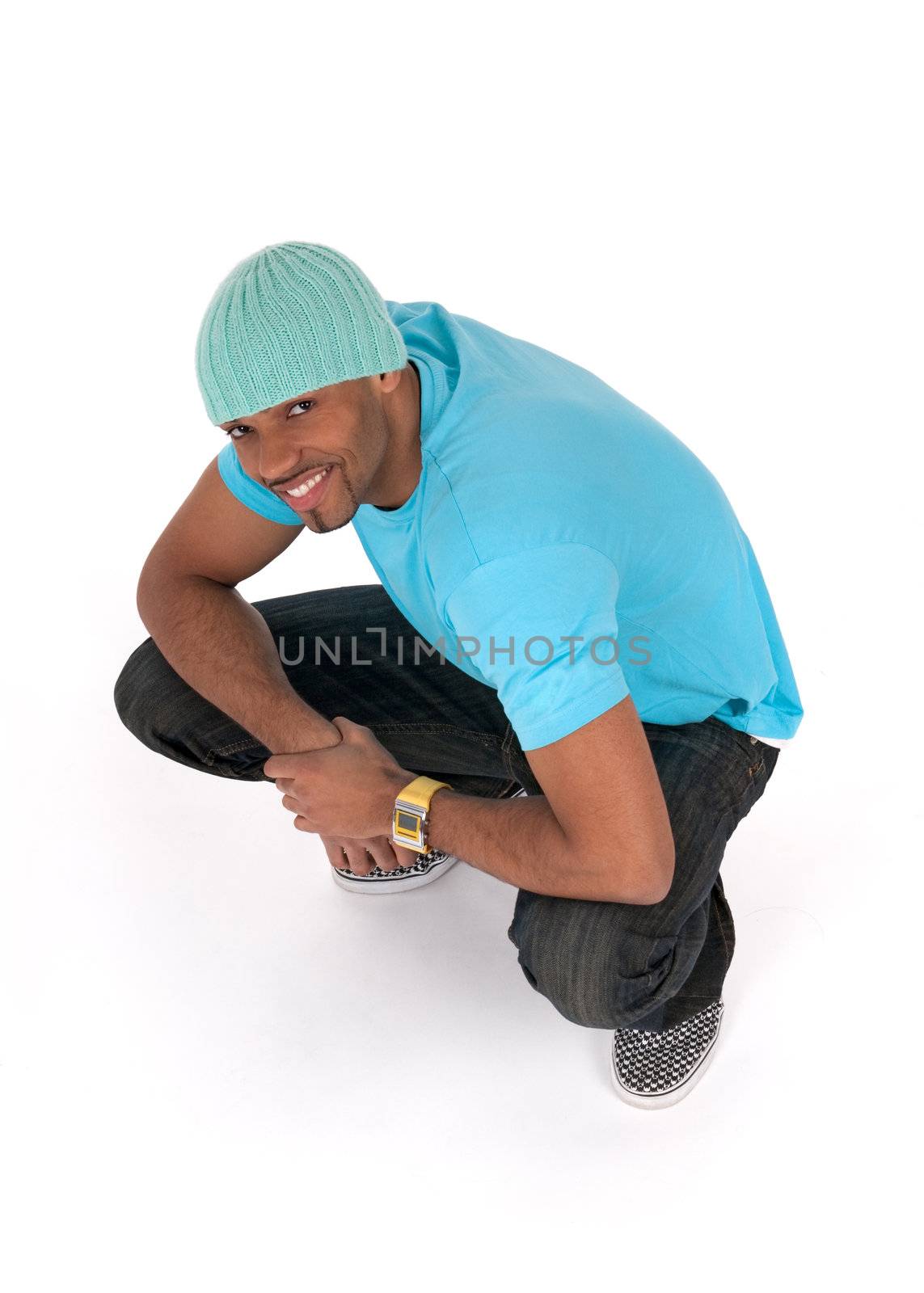 Smiling young man in a blue t-shirt squatting. Isolated on white background.