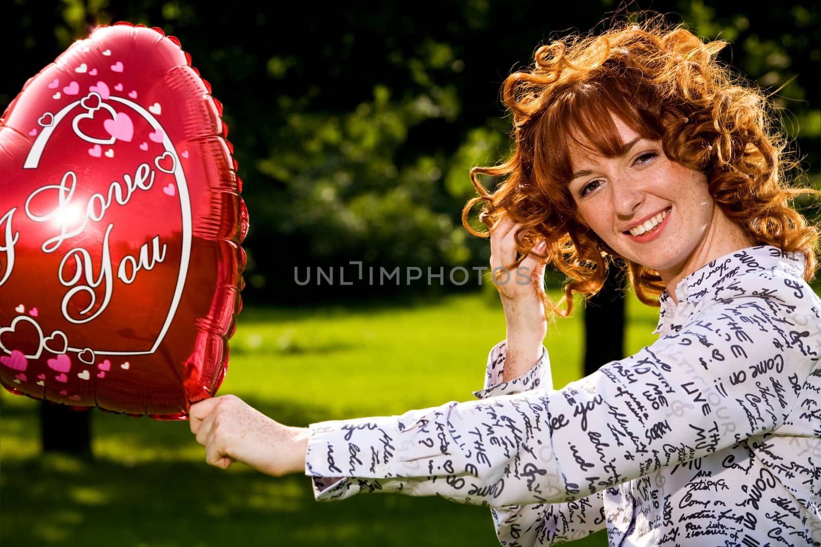 Red-haired lovely young woman holding red balloon in shape of heart outdoors 