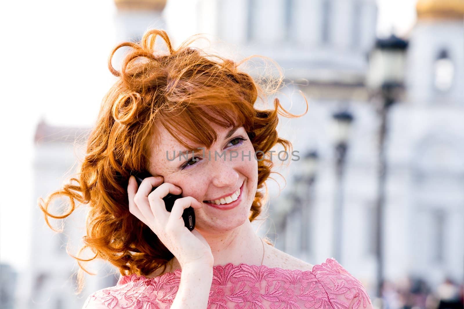 Smiling red-haired young woman talking on mobile phone outdoors