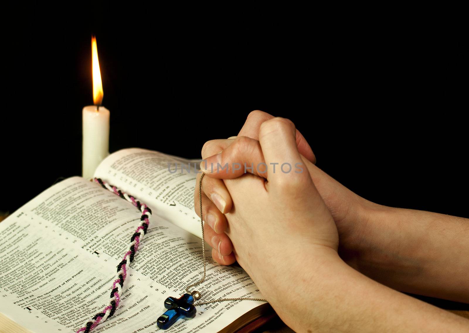 Open Bible with burning candle and hands of praying woman