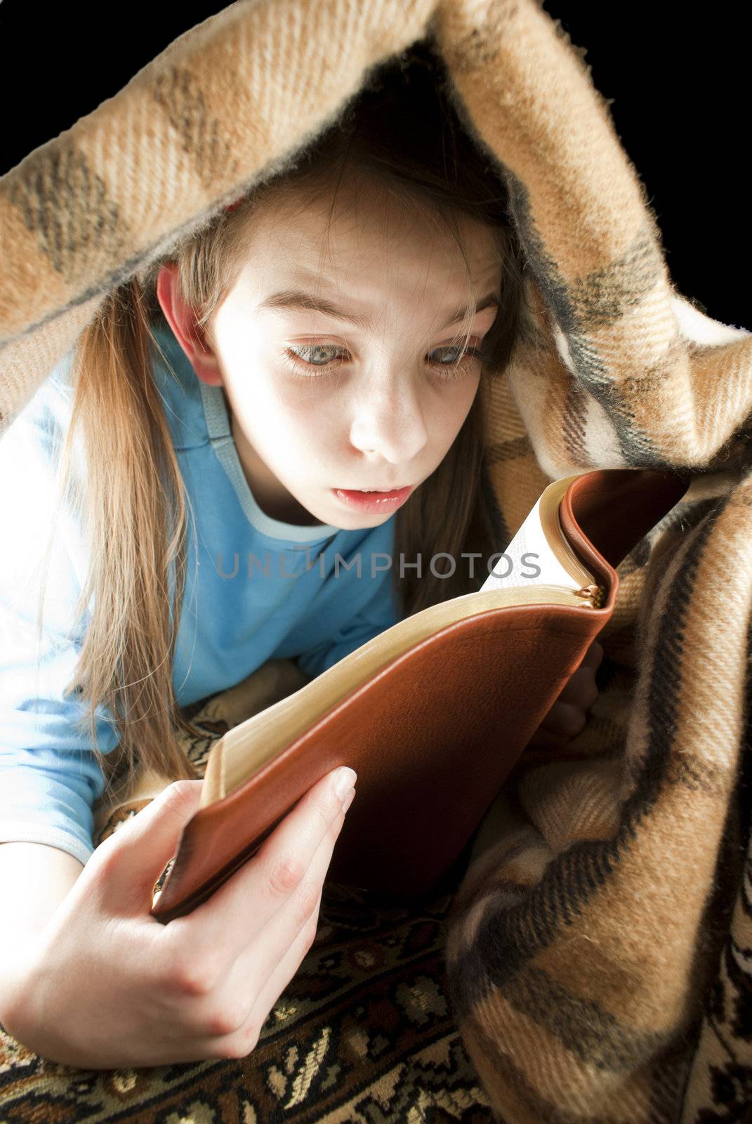Teen girl reading book hiding under blanket by AndreyKr