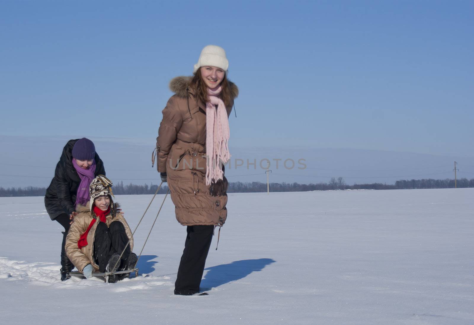 Three happy sisters sledding at winter time