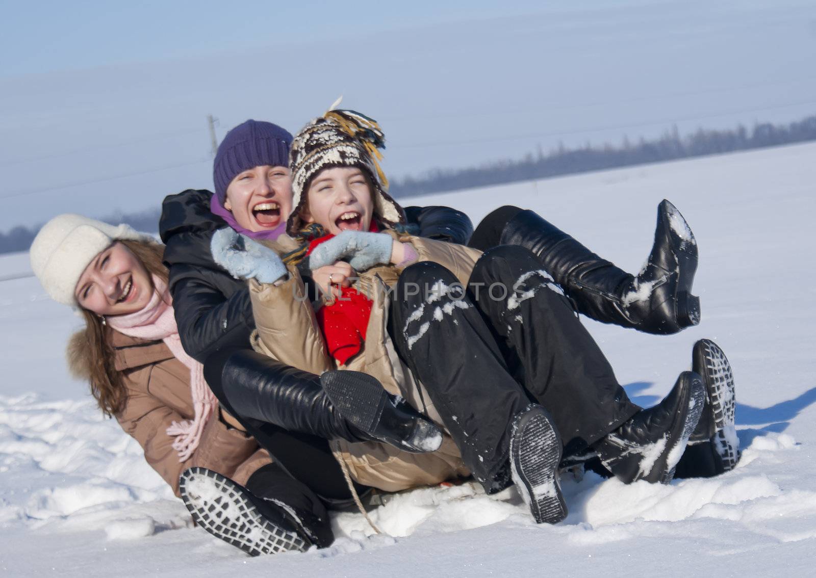 Three happy sisters sledding at winter time