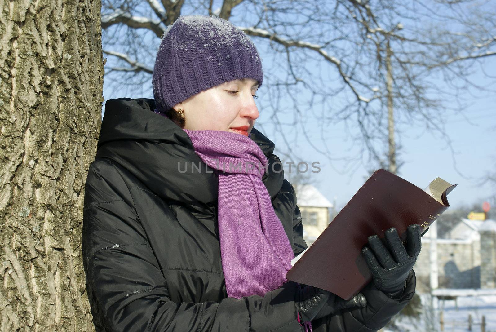 Young lady reading book outdoors at winter time