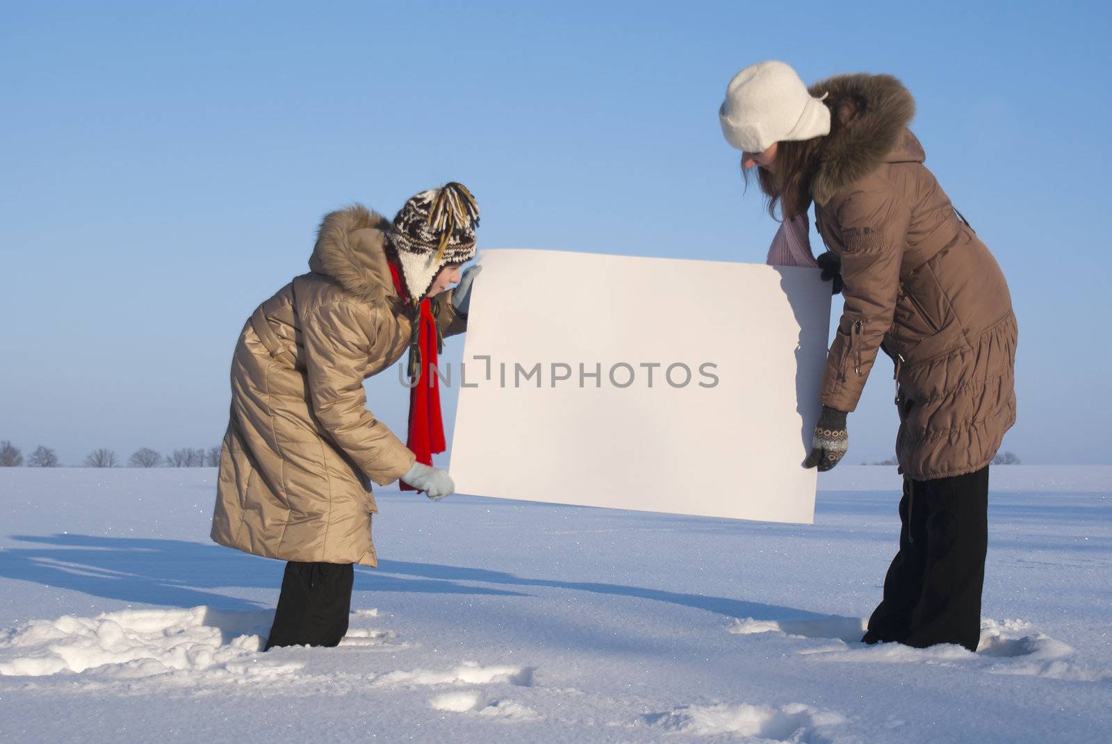 Girls holding white poster at winter snowy field by AndreyKr