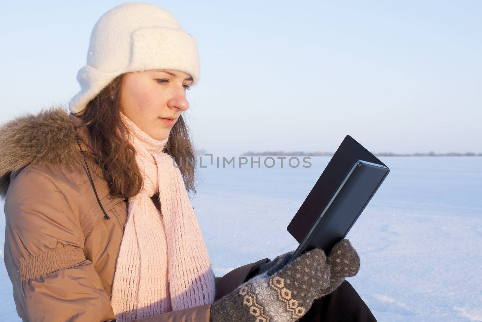 Teen girl reading e-book outdoors at winter time