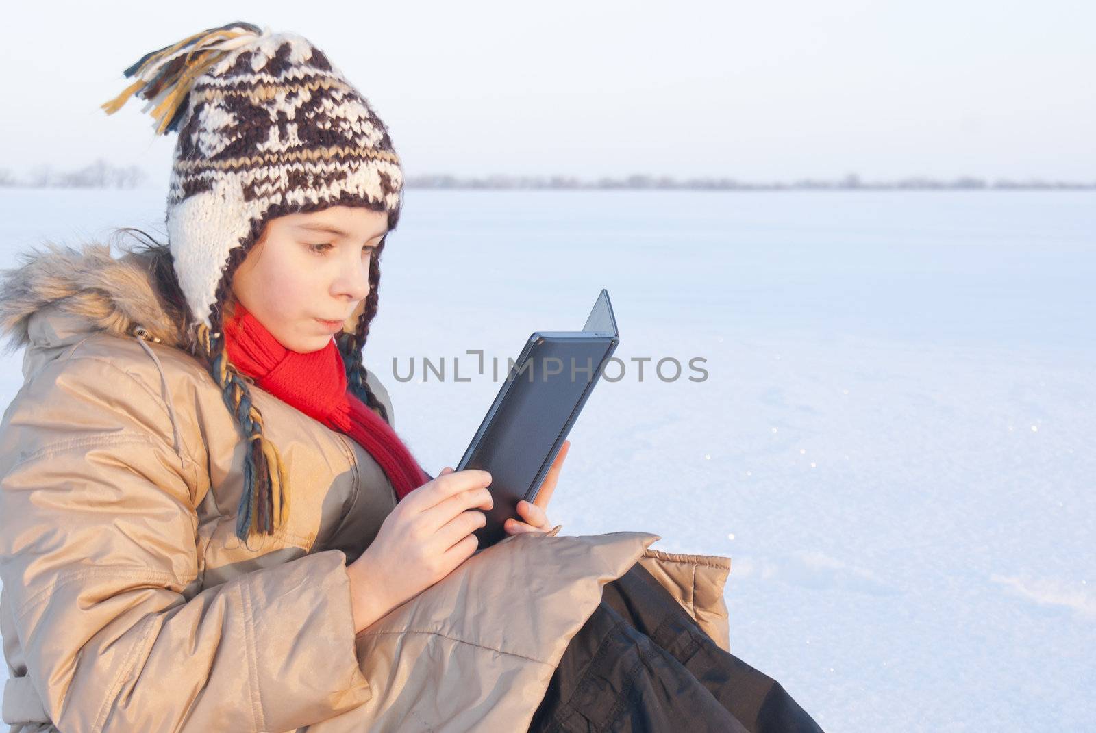 Teen girl reading e-book outdoors at winter time