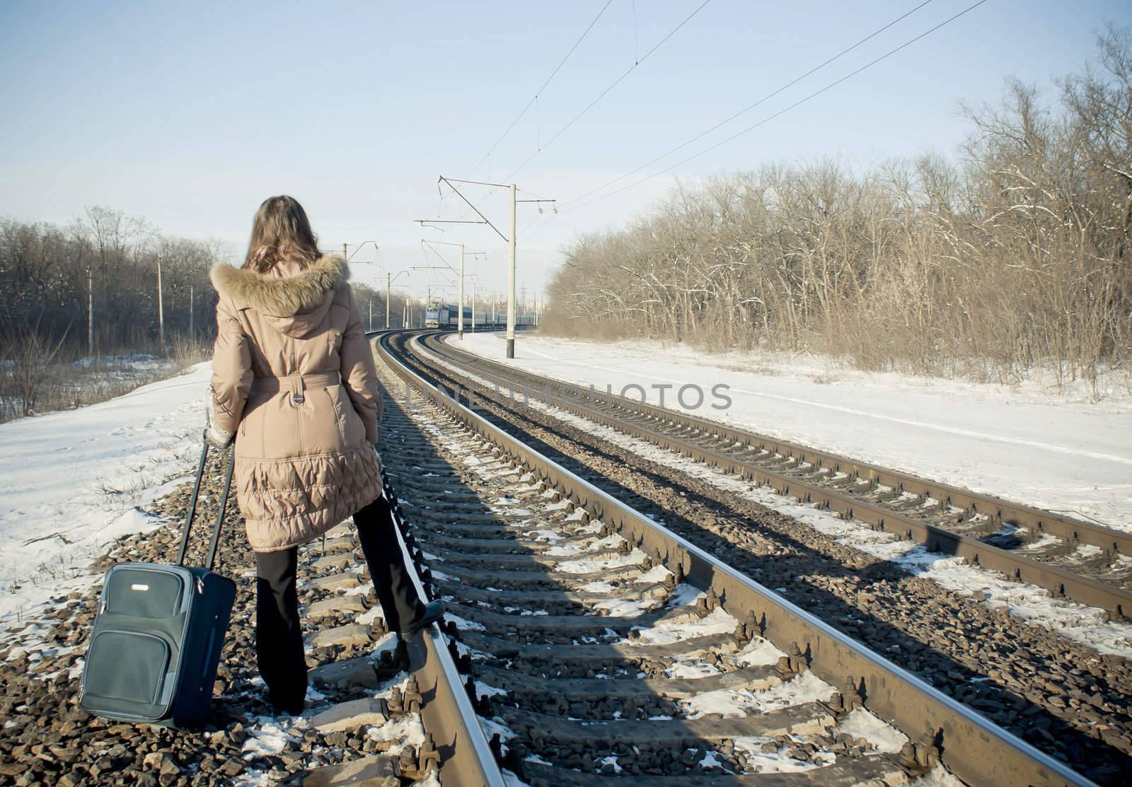 Teen girl with a suitcase near the railways at winter time