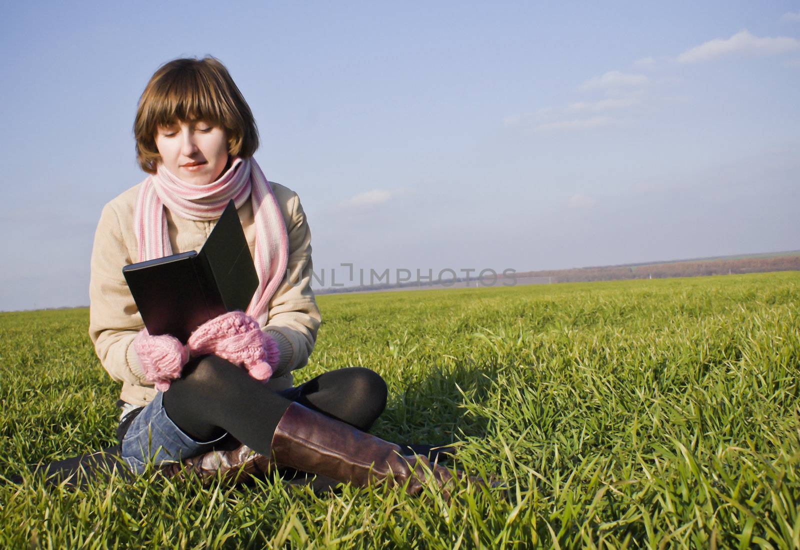Young lady reading a book sitting at grass by AndreyKr