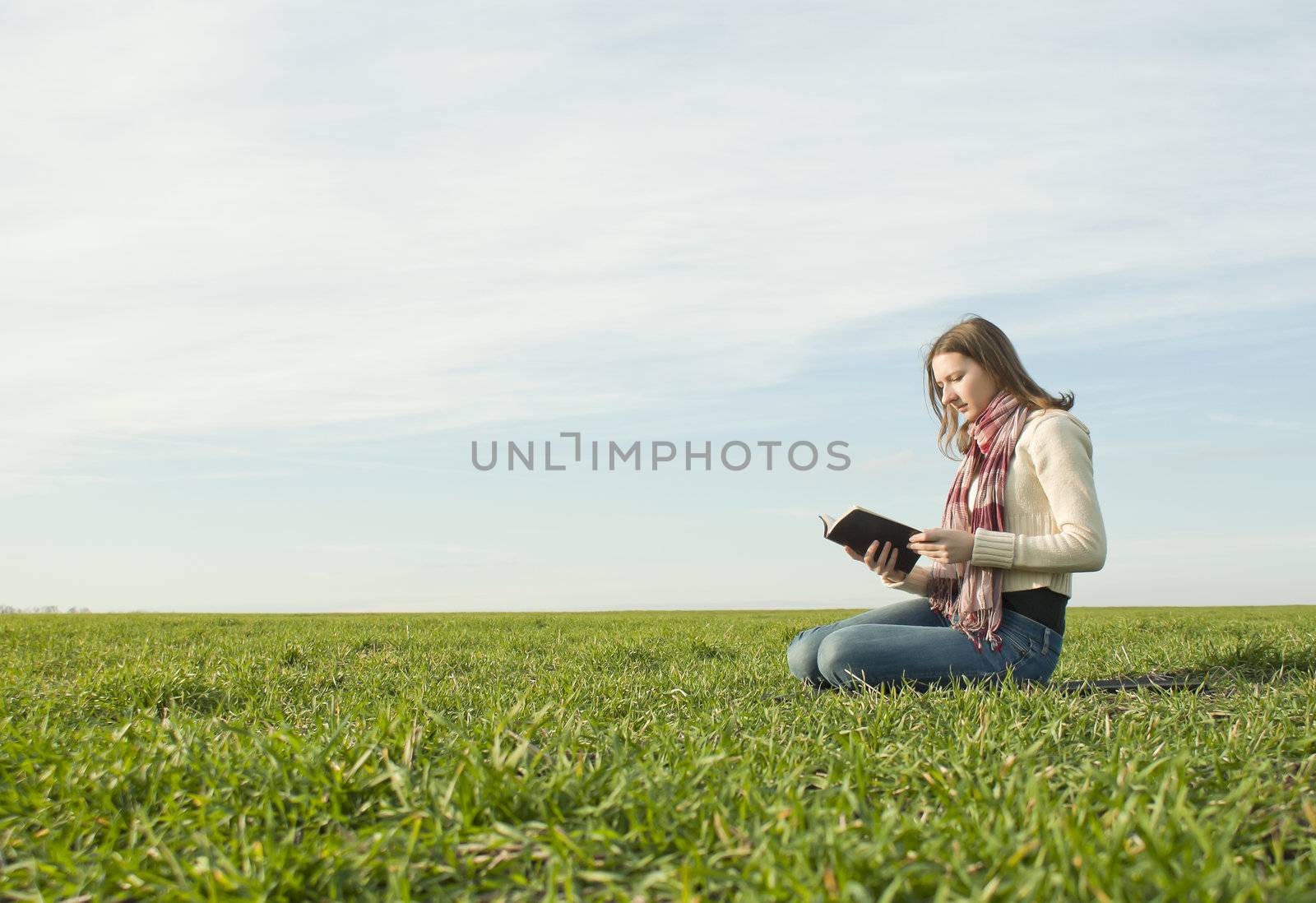 Teen girl reading a book sitting at grass by AndreyKr
