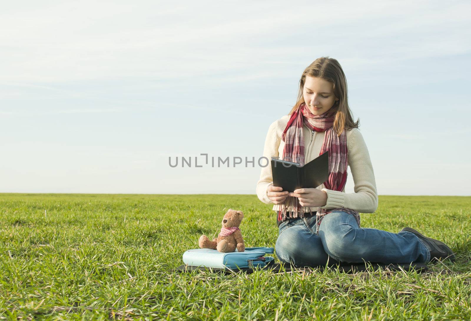 Girl reading a ebook sitting at grass by AndreyKr