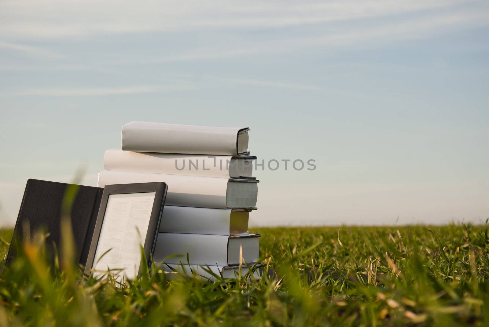Stack of books with ebook reader outdoors laying on grass by AndreyKr