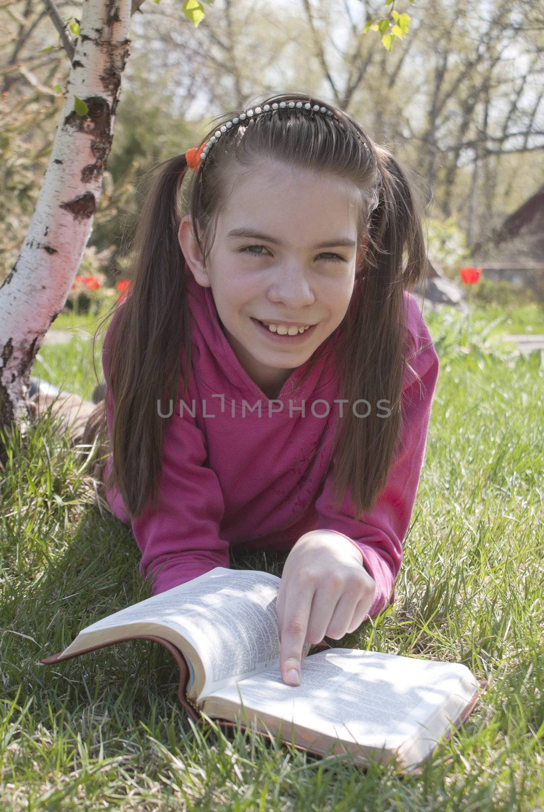 Teen girl reads book sitting on grass by AndreyKr
