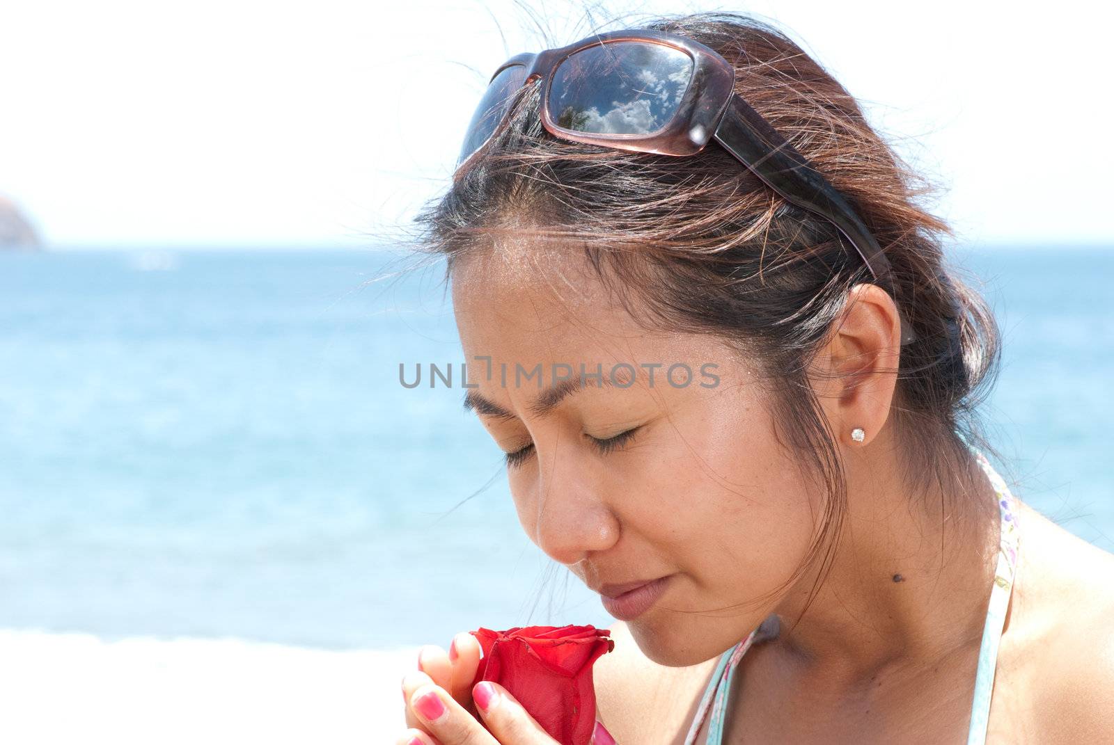 Beautiful oriental young lady smells a rose as she enjoys her vacations.