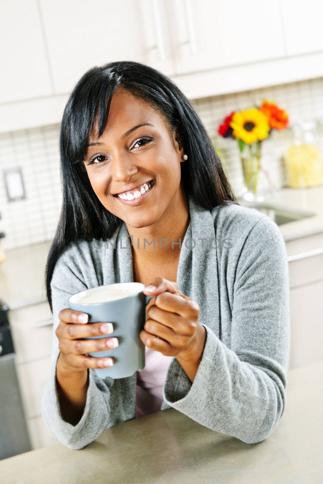 Smiling black woman holding coffee cup in modern kitchen interior