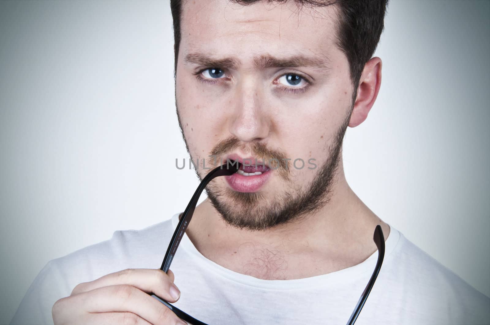 Young handsome man with blue eyes holding sunglasses in his mouth