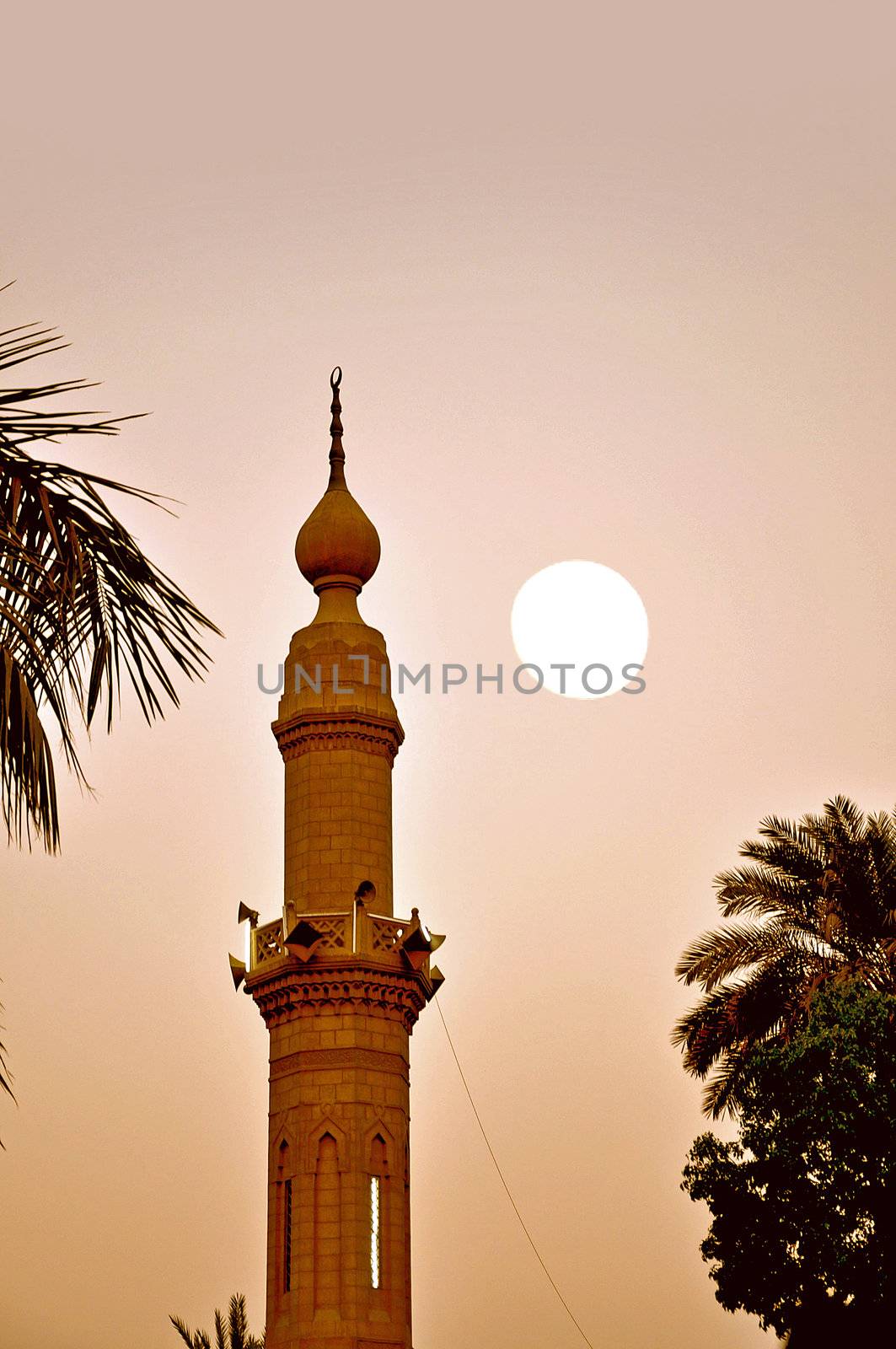 A sepia image of a minaret in Cairo and the moon in the background, sunset