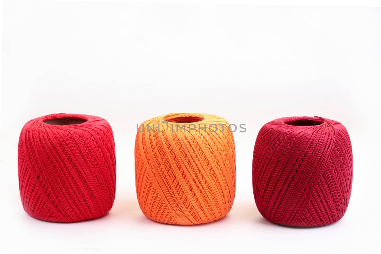 Red, yellow and purple coton spools against white background